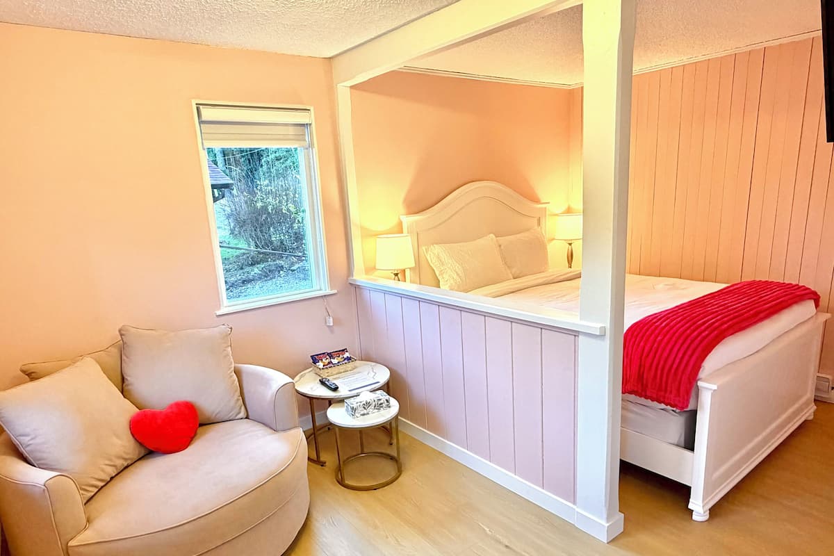A bedroom with a bed, a chair, a small table, and a window.