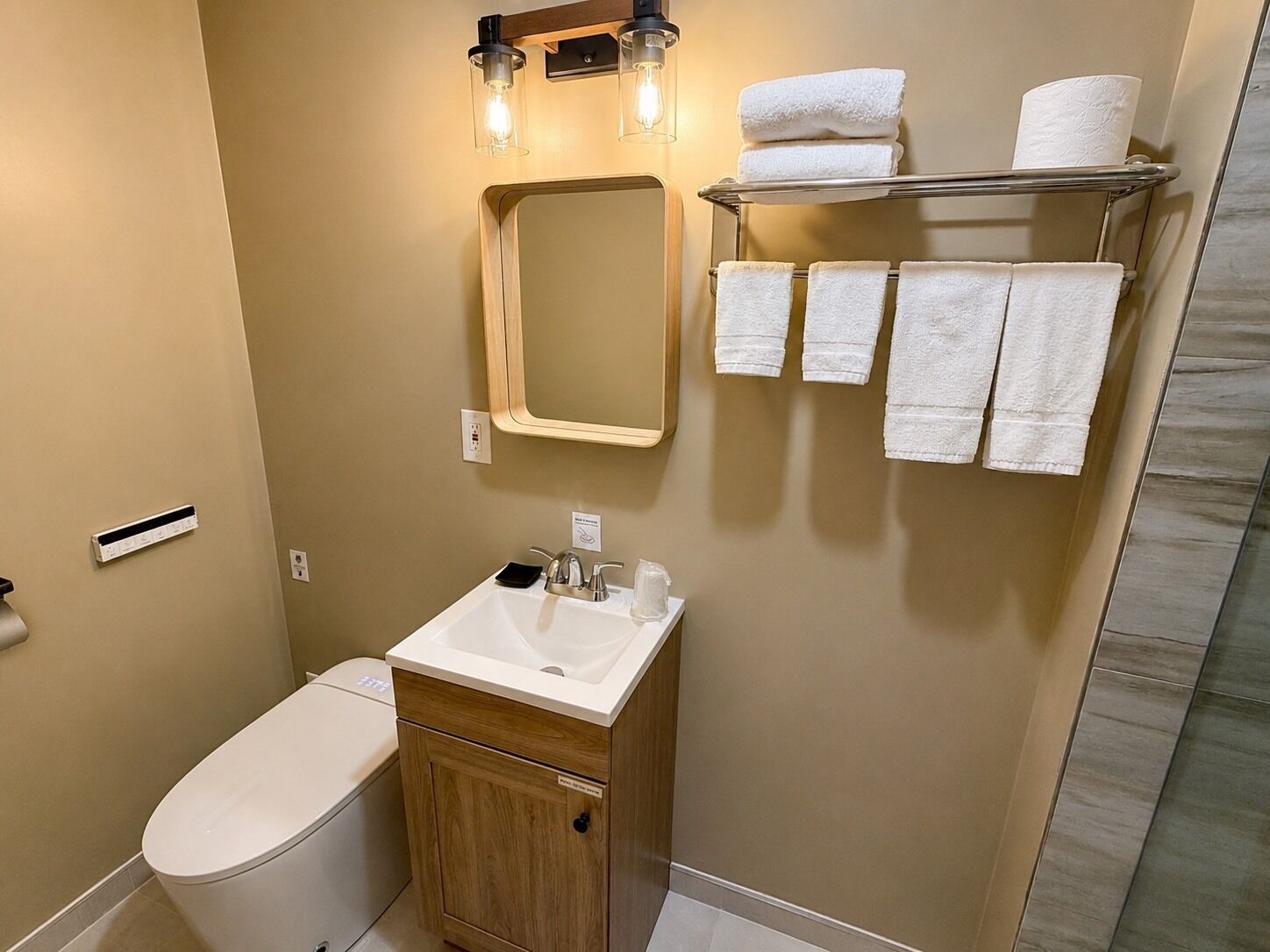 Un baño con inodoro, lavamanos, espejo, toallero y zona de ducha.