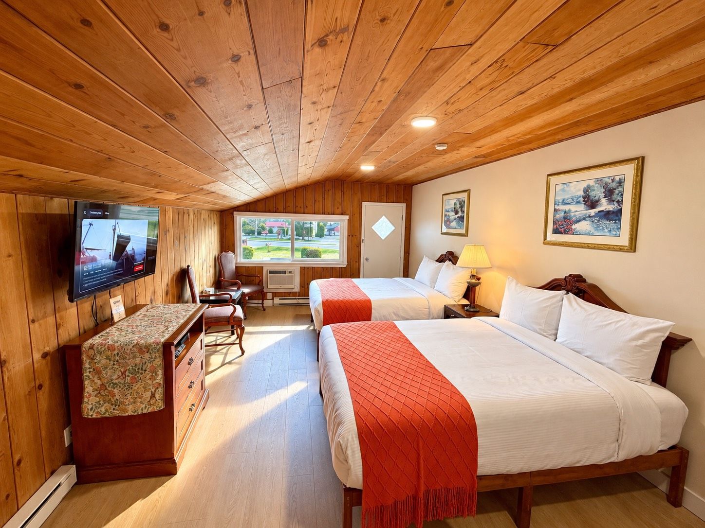 A cabin-style room with two beds, a television, a desk, and a chair.