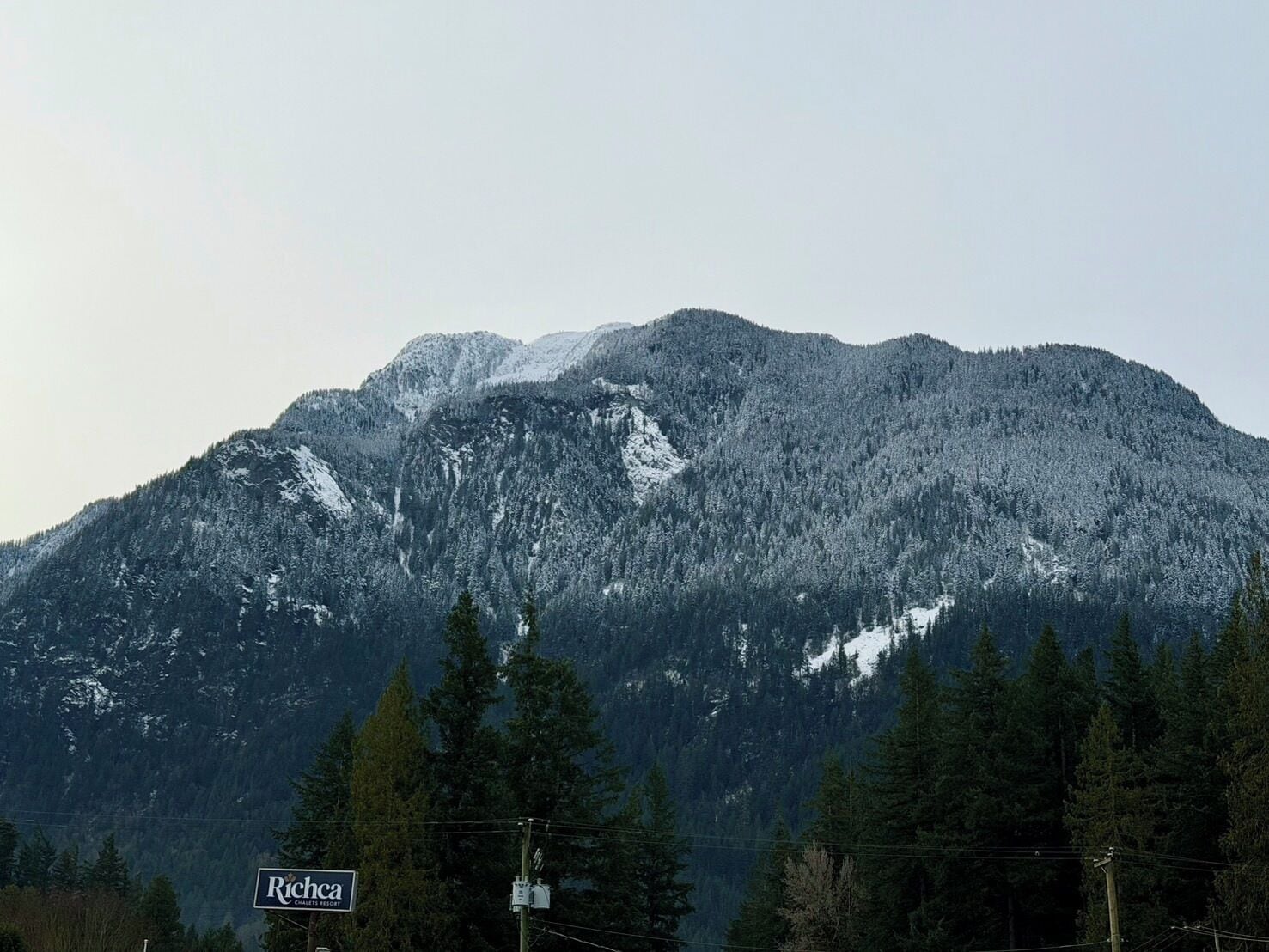 Ein Berg mit schneebedeckten Gipfeln und ein Schild für 'Richaca Chalet Resort' im Vordergrund.