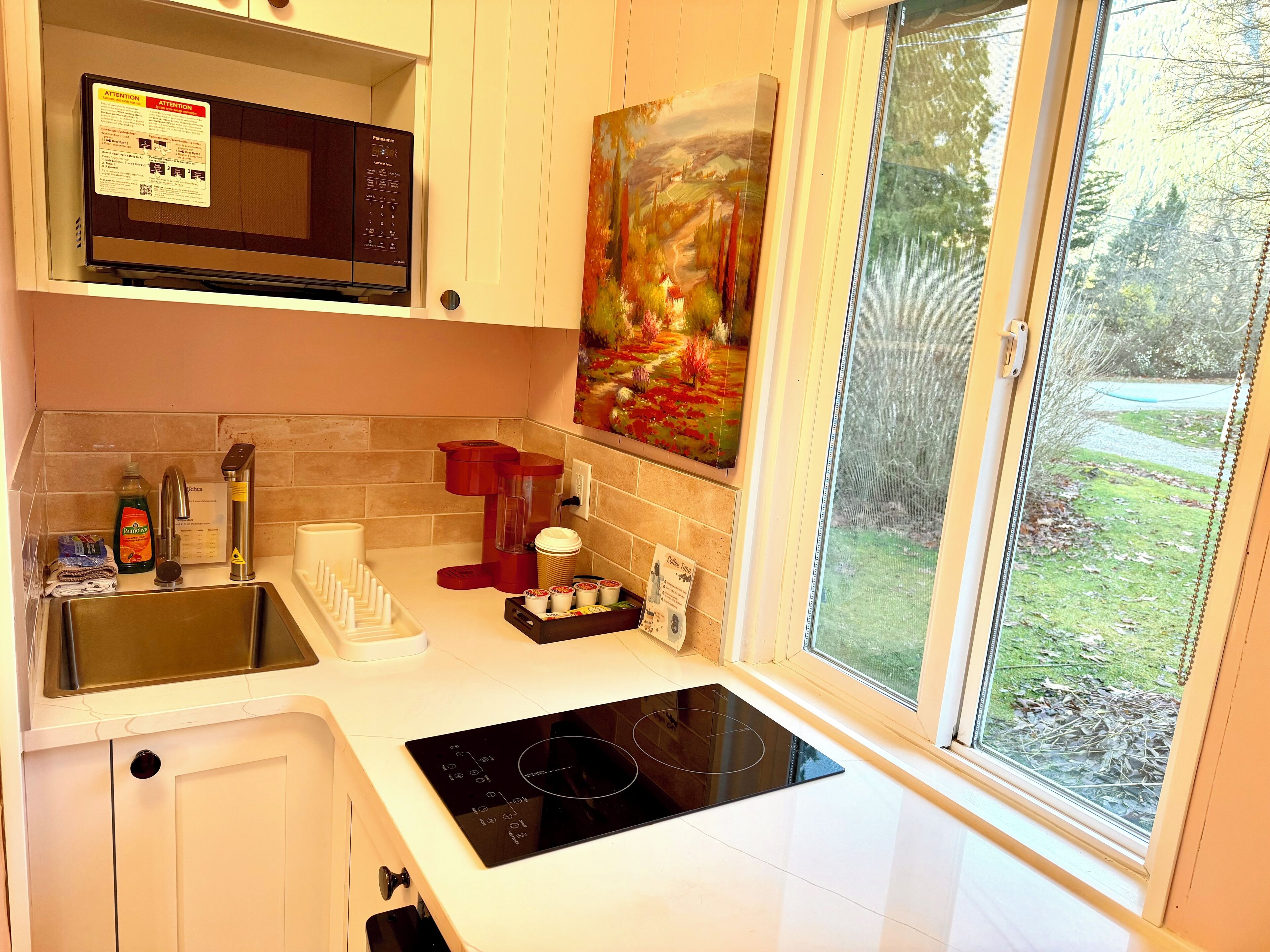 Een moderne keuken met een ingebouwde magnetron, koffiezetapparaat en een groot raam met uitzicht op het landschap.