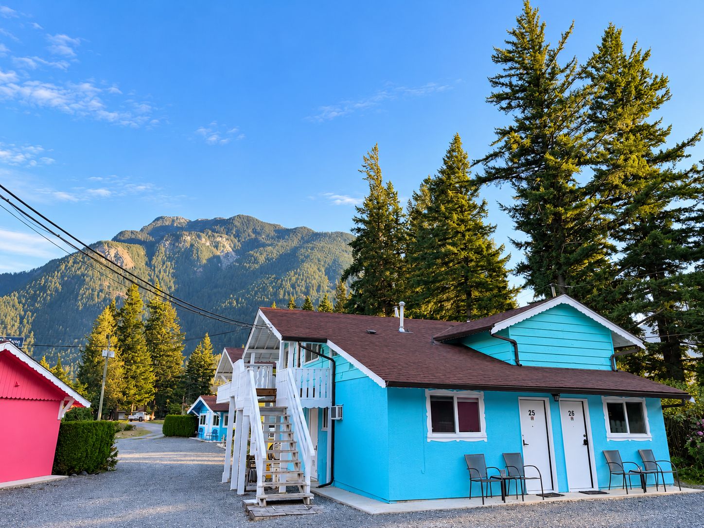 A two-story building with a staircase leading to the upper floor, a small porch with chairs, and a mountain backdrop.