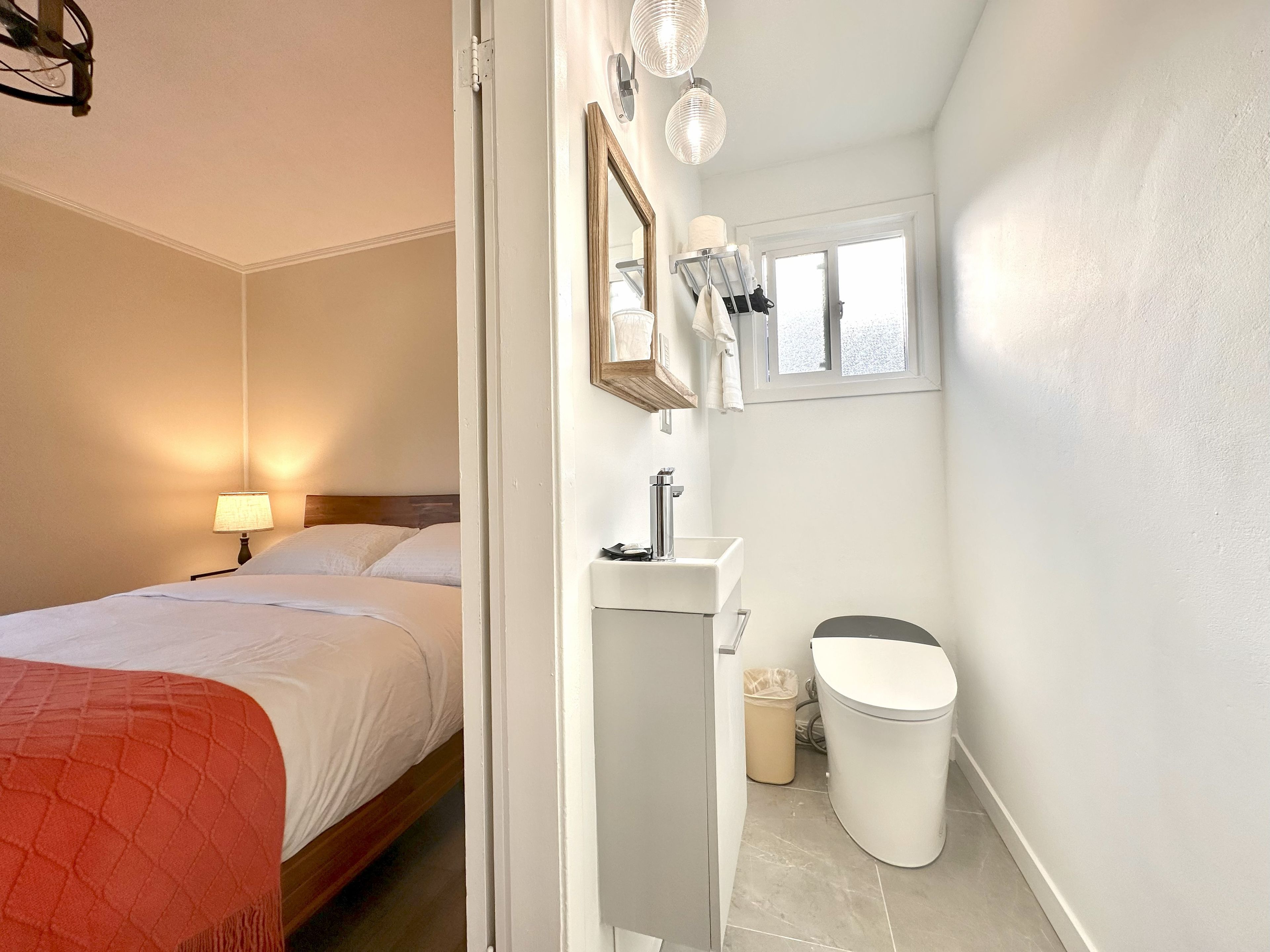 A hotel room with a bed, a bedside lamp, a bathroom with a sink, mirror, and toilet.
