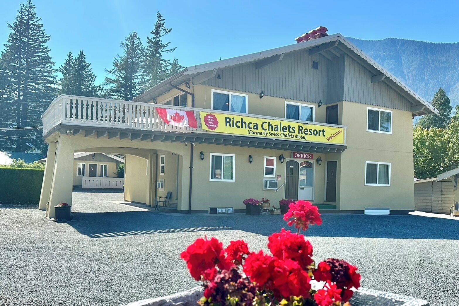 Un bâtiment à deux étages doté d’un balcon, d’une enseigne indiquant « Richca Chalets Resort », et ayant une chaîne de montagnes en arrière-plan.
