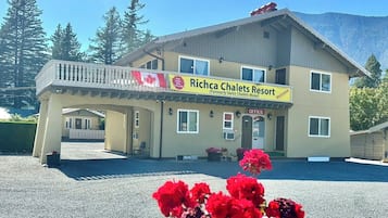 Un edificio de dos pisos con un balcón, un cartel que dice 'Richca Chalets Resort' y un paisaje montañoso al fondo.