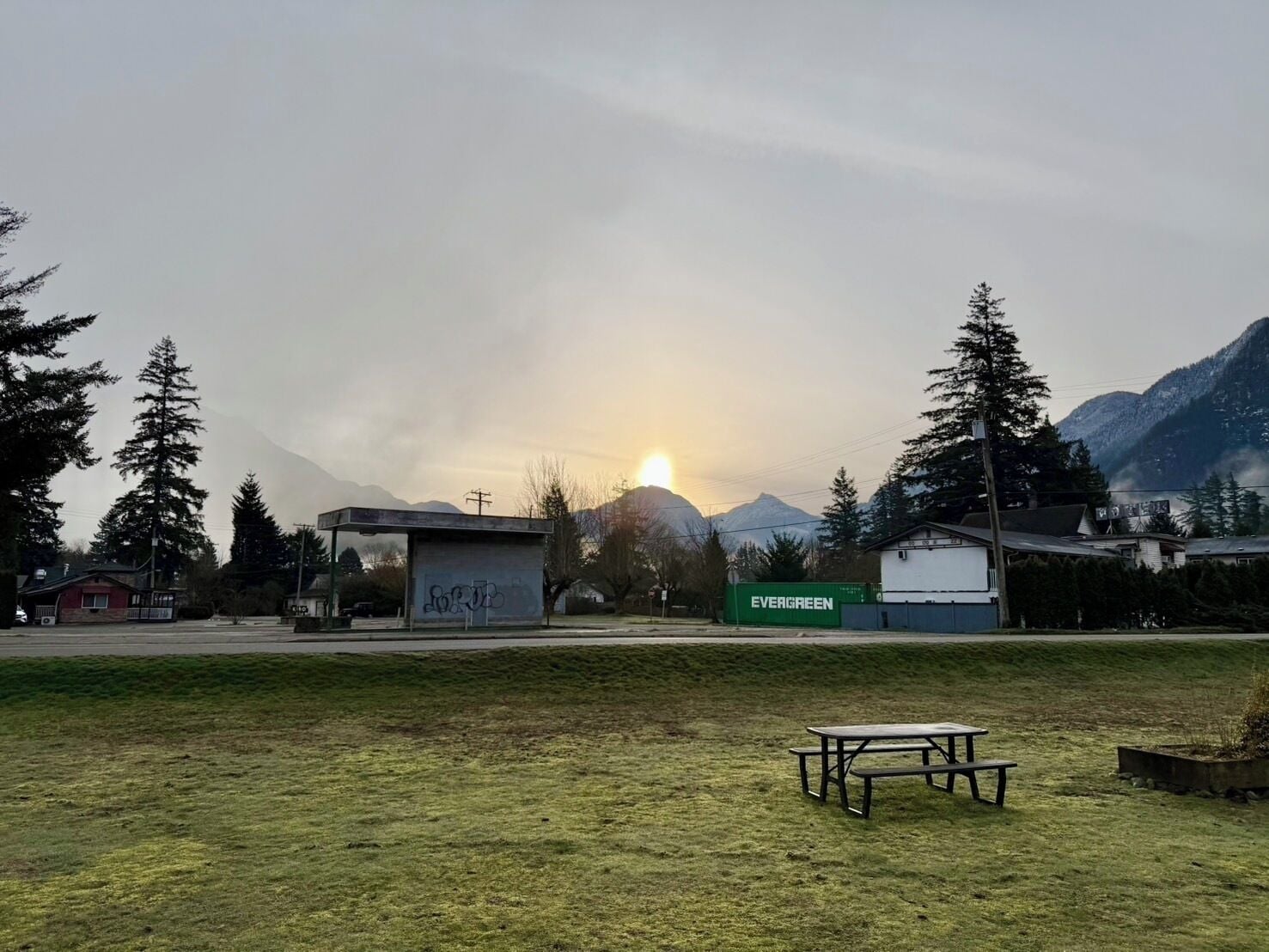 Un campo cubierto de hierba con una mesa de picnic, un pequeño edificio con grafitis y un letrero verde para Evergreen.