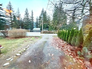 A gravel driveway leading to a house with a white picket fence, surrounded by evergreen trees and a small garden. - Richca Chalets Resort (Hope)