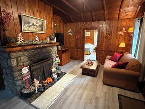 A cozy living room with a stone fireplace, wooden walls, a sofa, and a television. - Richca Chalets Resort (Hope)