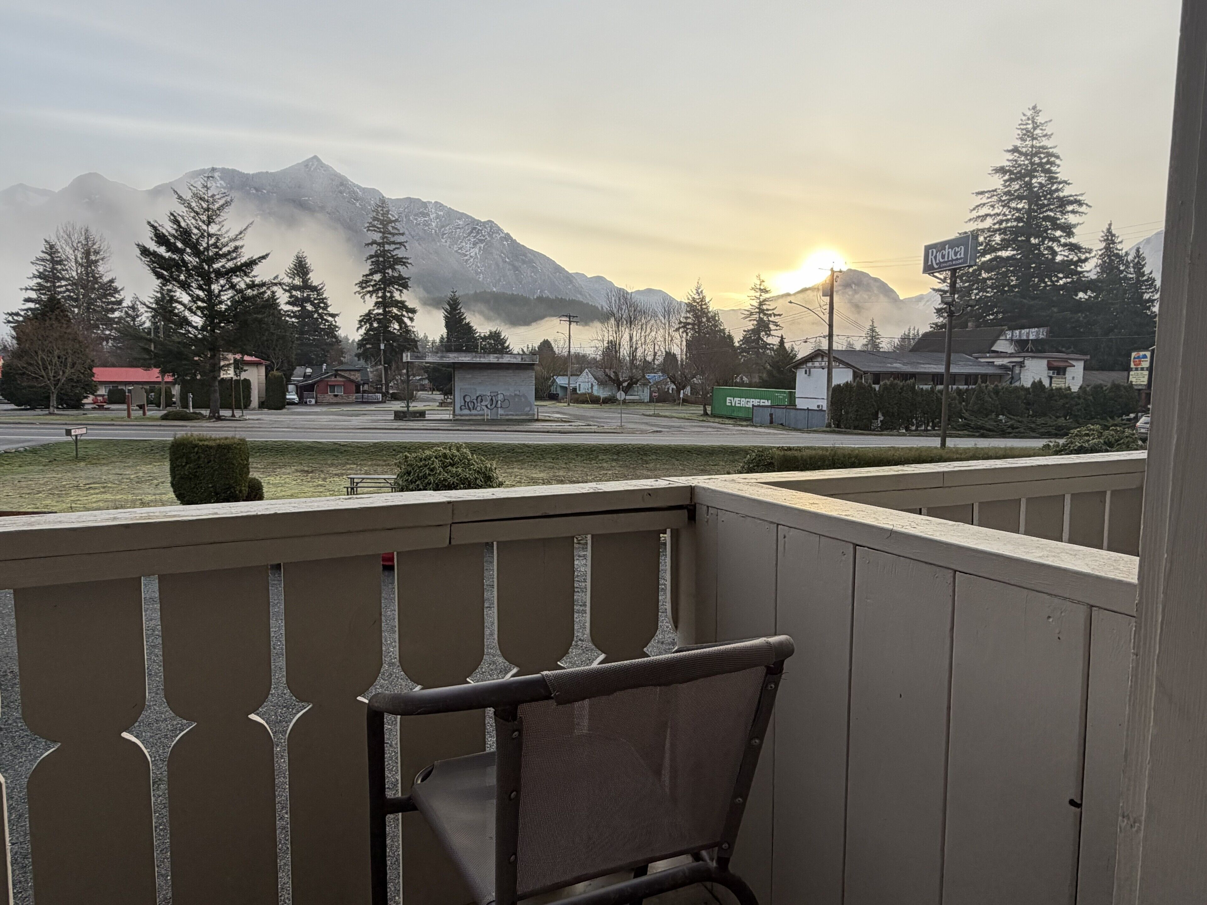 A balcony with a chair, a view of a street, houses, and mountains in the background.