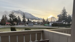 Un balcon avec une chaise, donnant sur une rue, des maisons et, au loin, des montagnes.