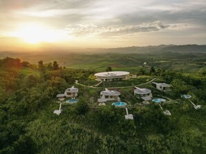 Un resort lujoso con varias construcciones circulares, cada una con piscina, en un paisaje verde exuberante y una vista panorámica de colinas ondulantes.