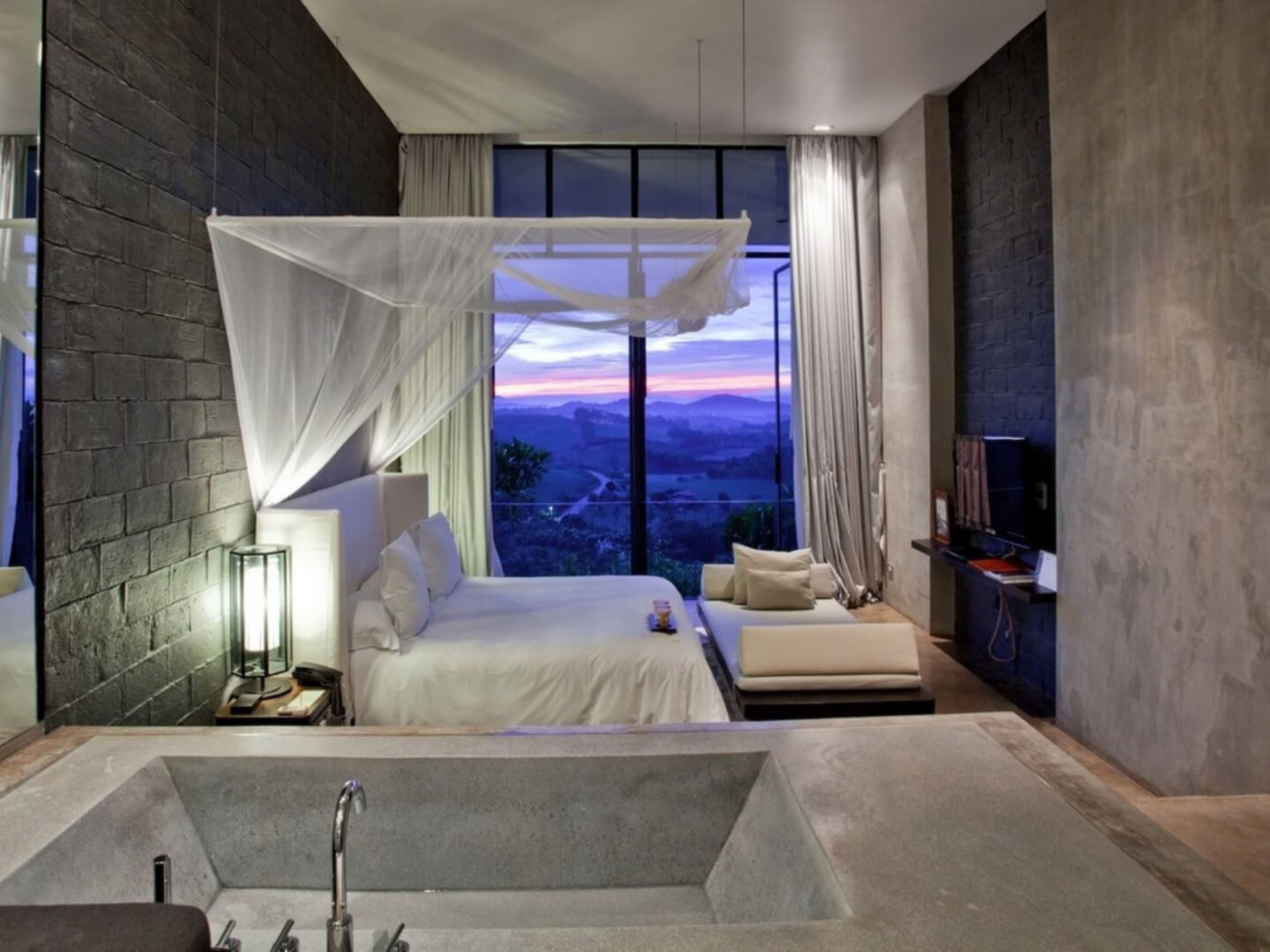 A modern bedroom with a large bed, a view of the landscape, and a separate bathroom area.