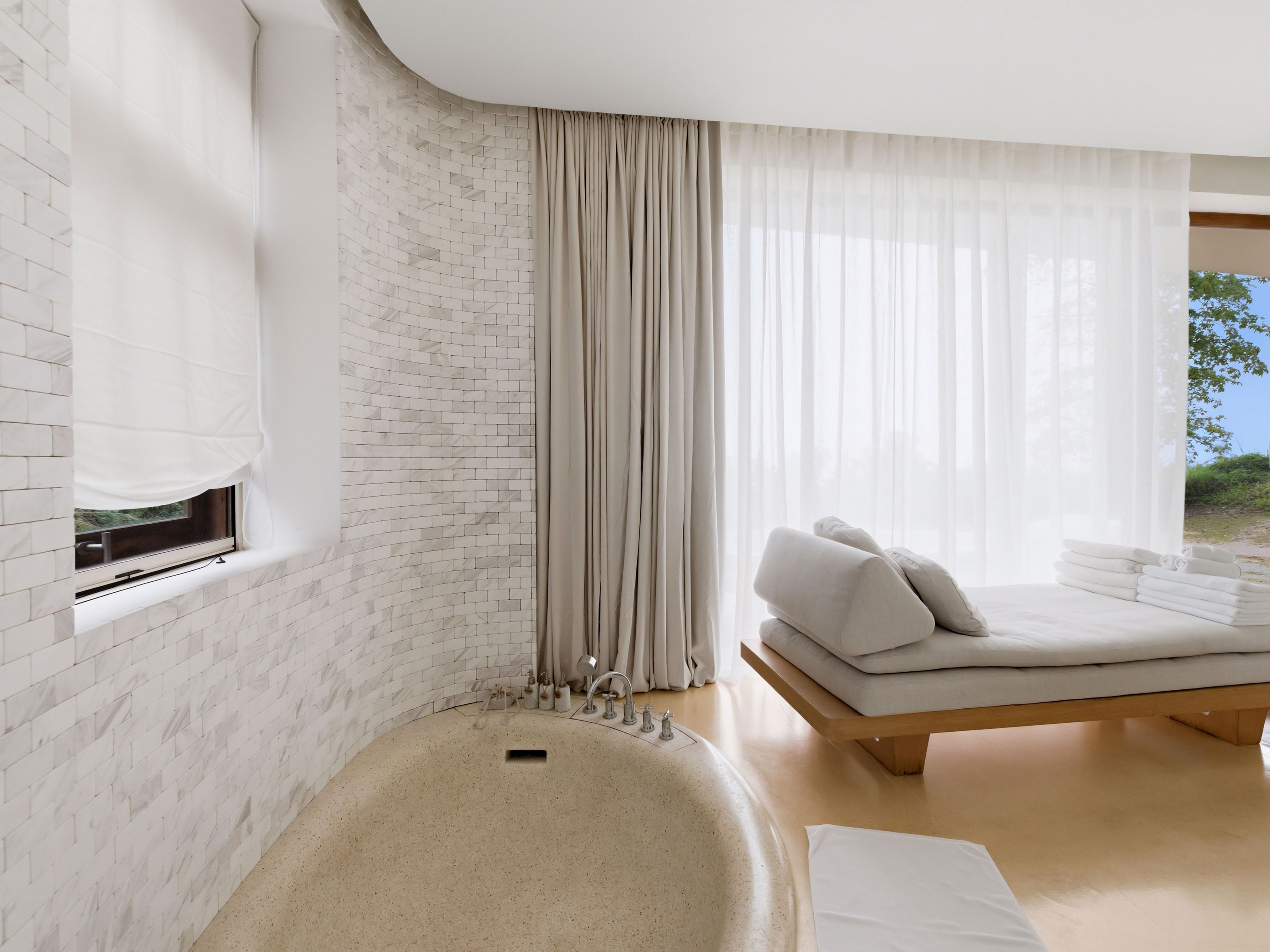 A modern bathroom with a freestanding bathtub, a window with a view, and a bed with a view.
