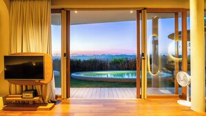 A room with a TV, a fan, and a view of a pool and landscape. - Sala Khaoyai (Pak Chong)