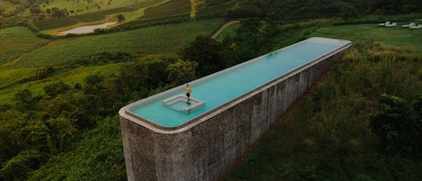 Ein rechteckiger Pool, in dessen Mitte eine Person steht, umgeben von üppiger Vegetation und Hügeln im Hintergrund.