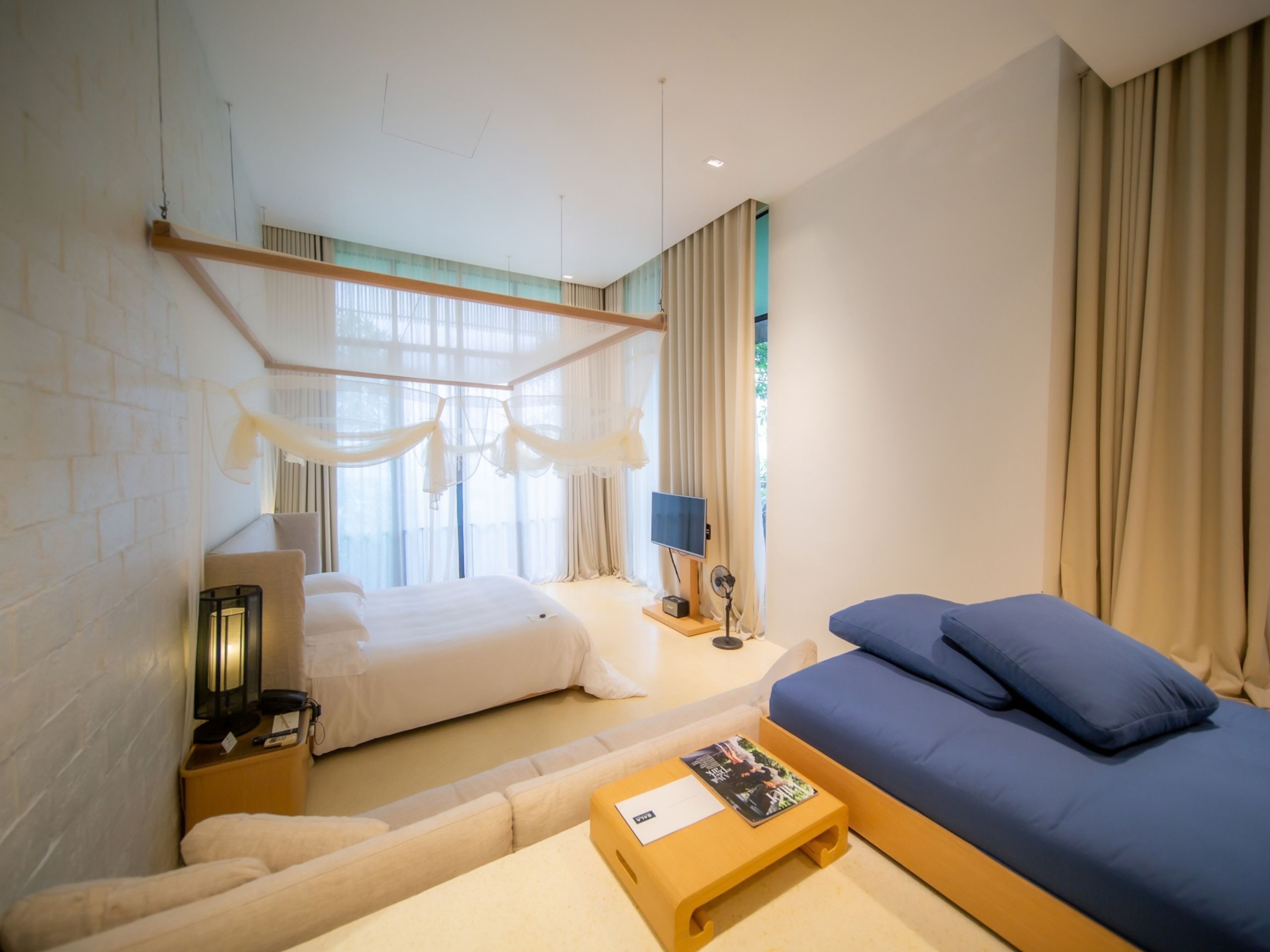 A hotel room with a bed, a sofa, a bedside table, a lamp, and a window with curtains.