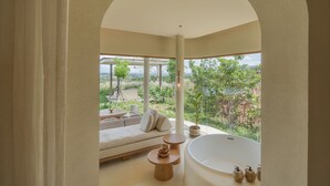 A modern bathroom with a large bathtub, a sofa, and a view of a lush garden. - Sala Khaoyai (Pak Chong)