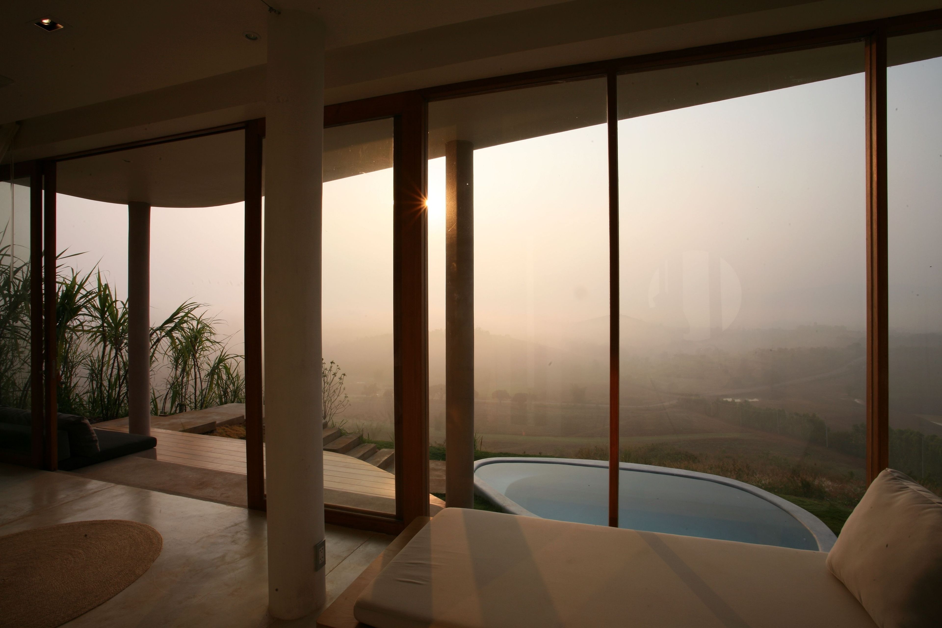 A modern living room with a large glass wall, a pool, and a view of a hilly landscape.