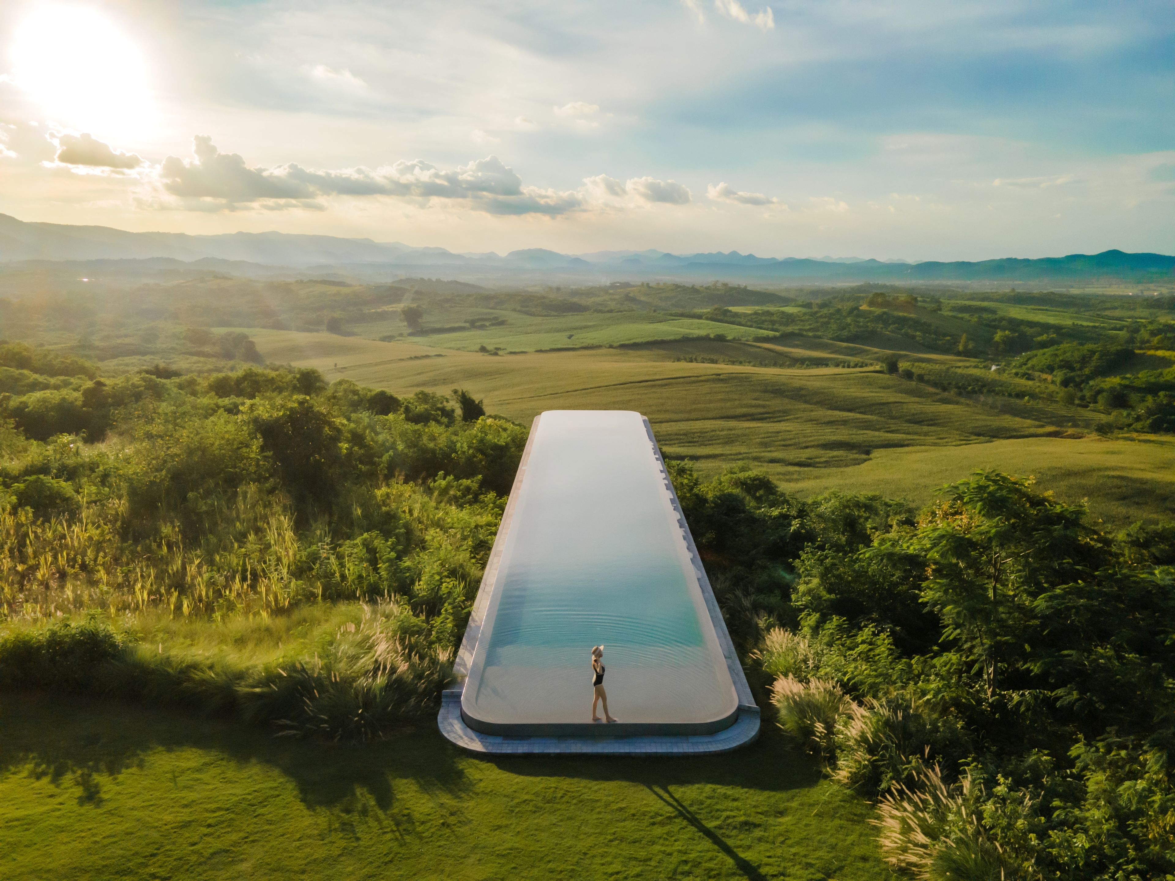 A person standing in a large, rectangular pool with a view of rolling hills and a clear sky.