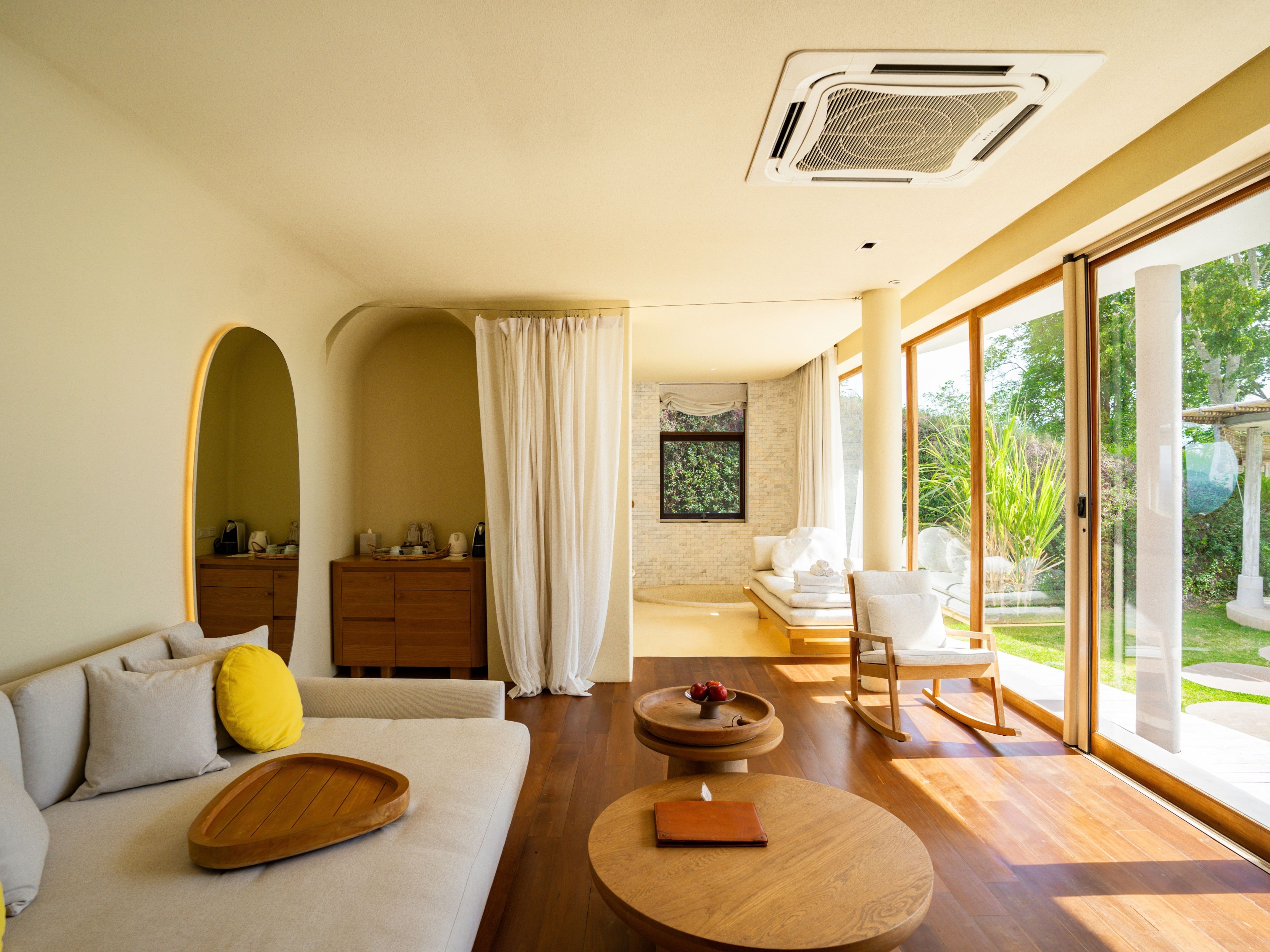 Um interior moderno com sofá, mesa de madeira e vista para o exterior por grandes portas de vidro.