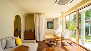 Um interior moderno com sofá, mesa de madeira e vista para o exterior por grandes portas de vidro.