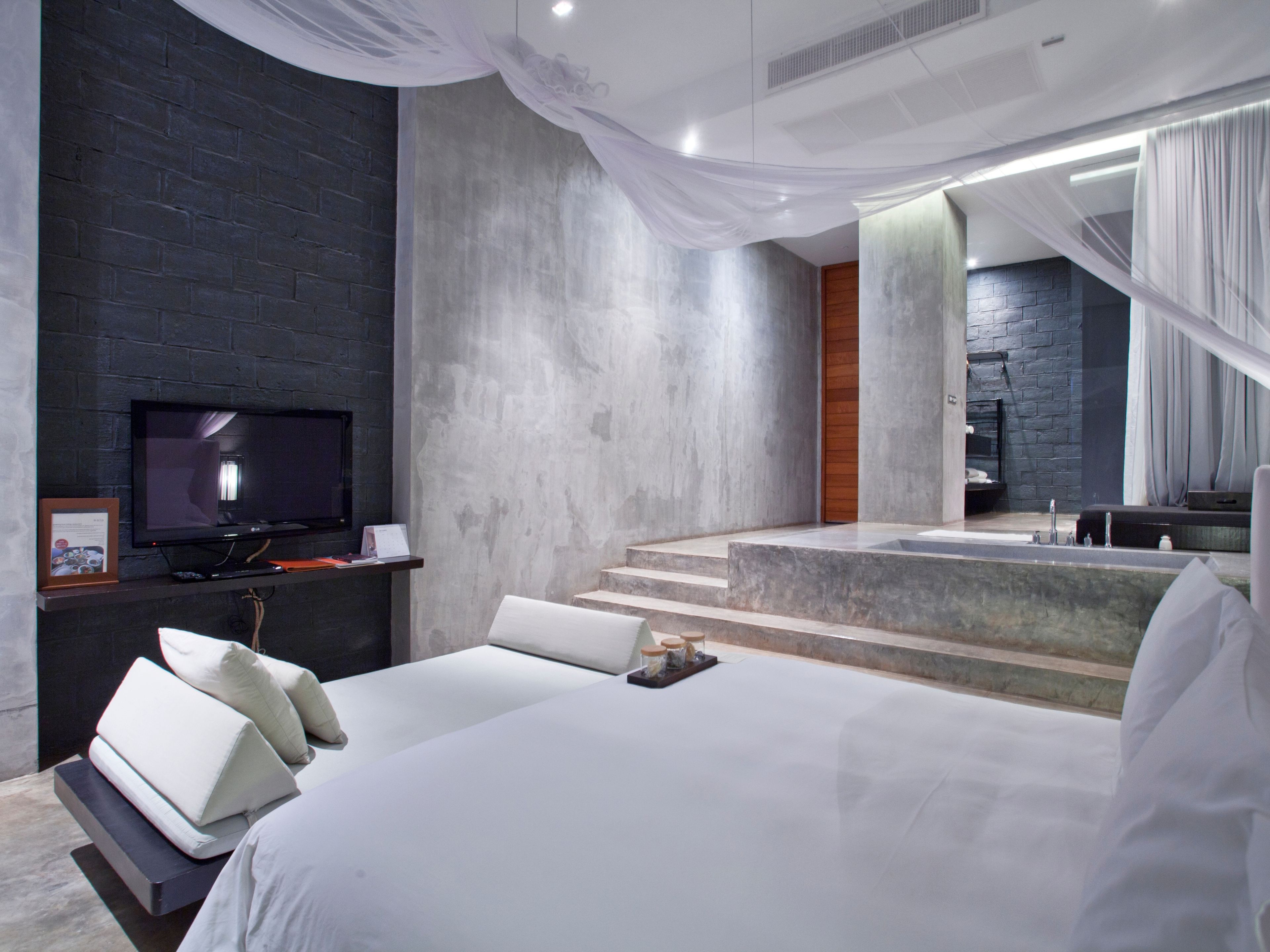 A modern hotel room with a large bed, a flat-screen TV, and a stone wall.