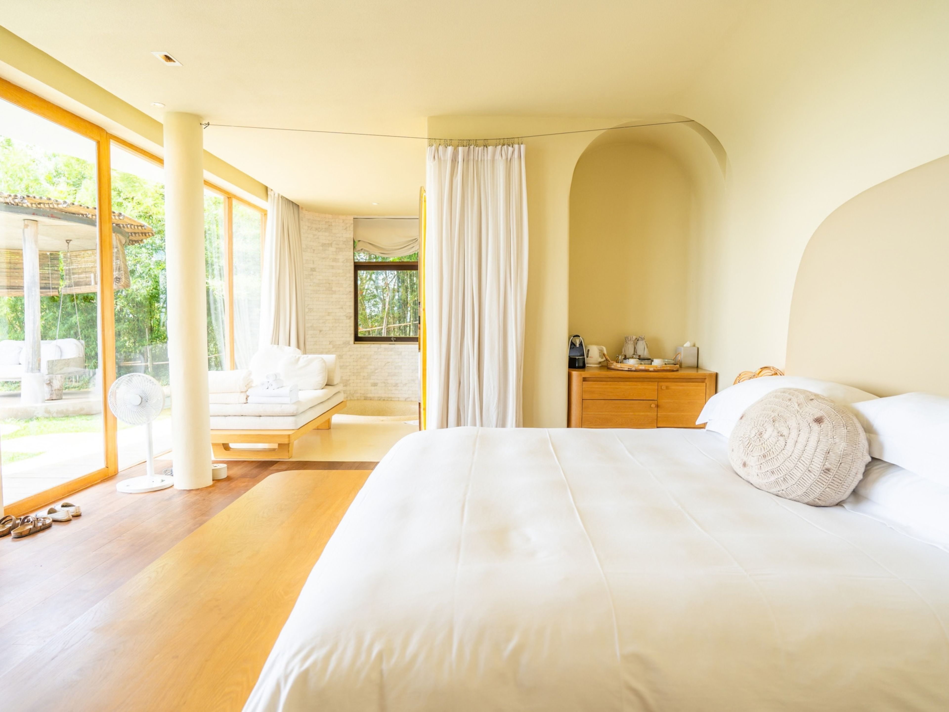 Une chambre à coucher moderne avec un grand lit, une table de chevet en bois et une vue sur l’extérieur.