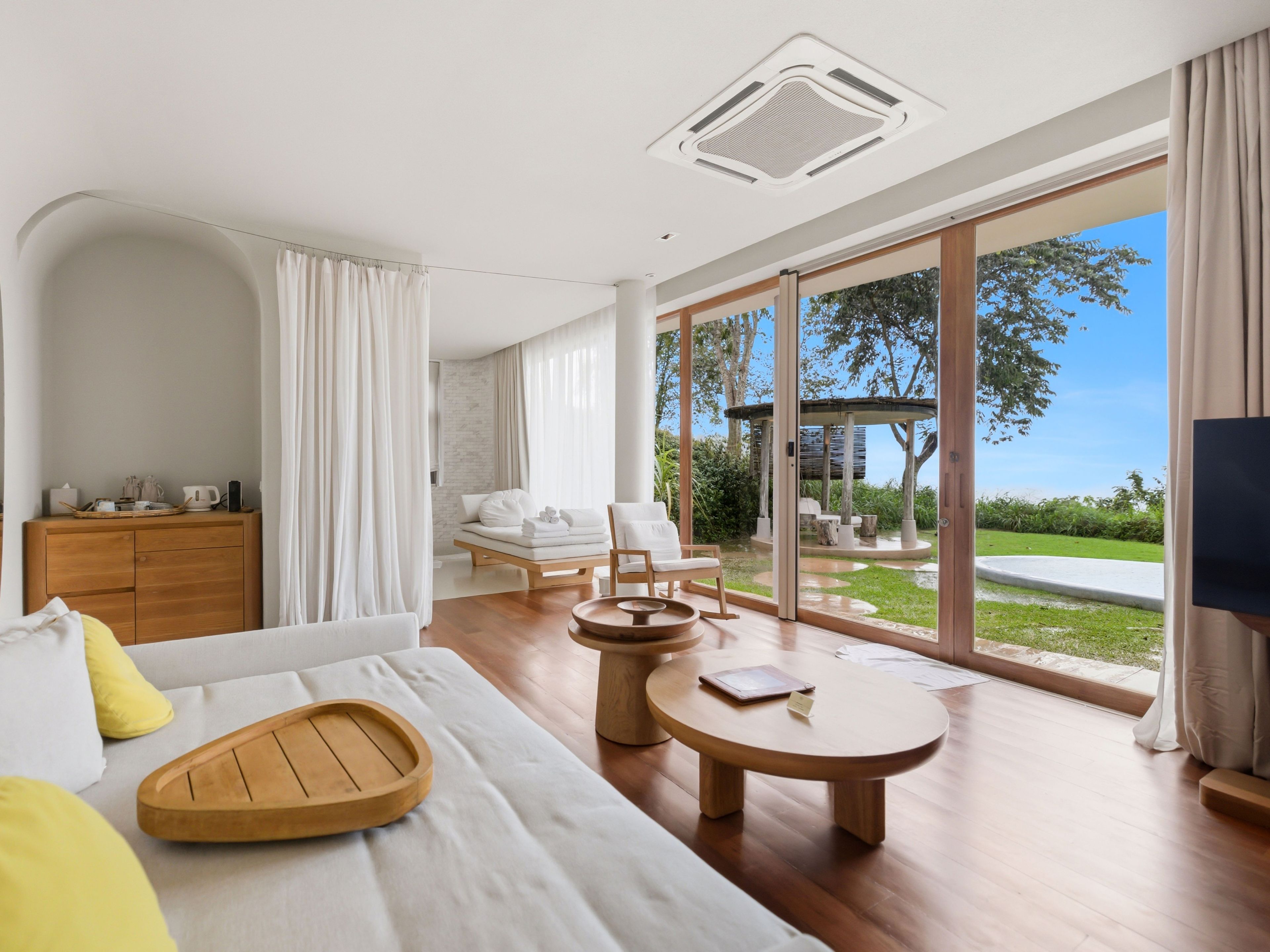 A modern hotel room with a large bed, a wooden side table, a sofa, a small round table, and a TV.
