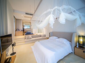 A modern hotel room with a large bed, a sitting area with a sofa and a coffee table, a TV, and a bedside table with a lamp. - Sala Khaoyai (Pak Chong)