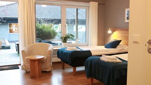 Habitación de hotel con dos camas, una mesita, una silla y un amplio ventanal con vistas al exterior.