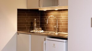 Una cocina compacta con muebles blancos, un salpicadero de azulejos negros y un lavamanos de acero inoxidable.