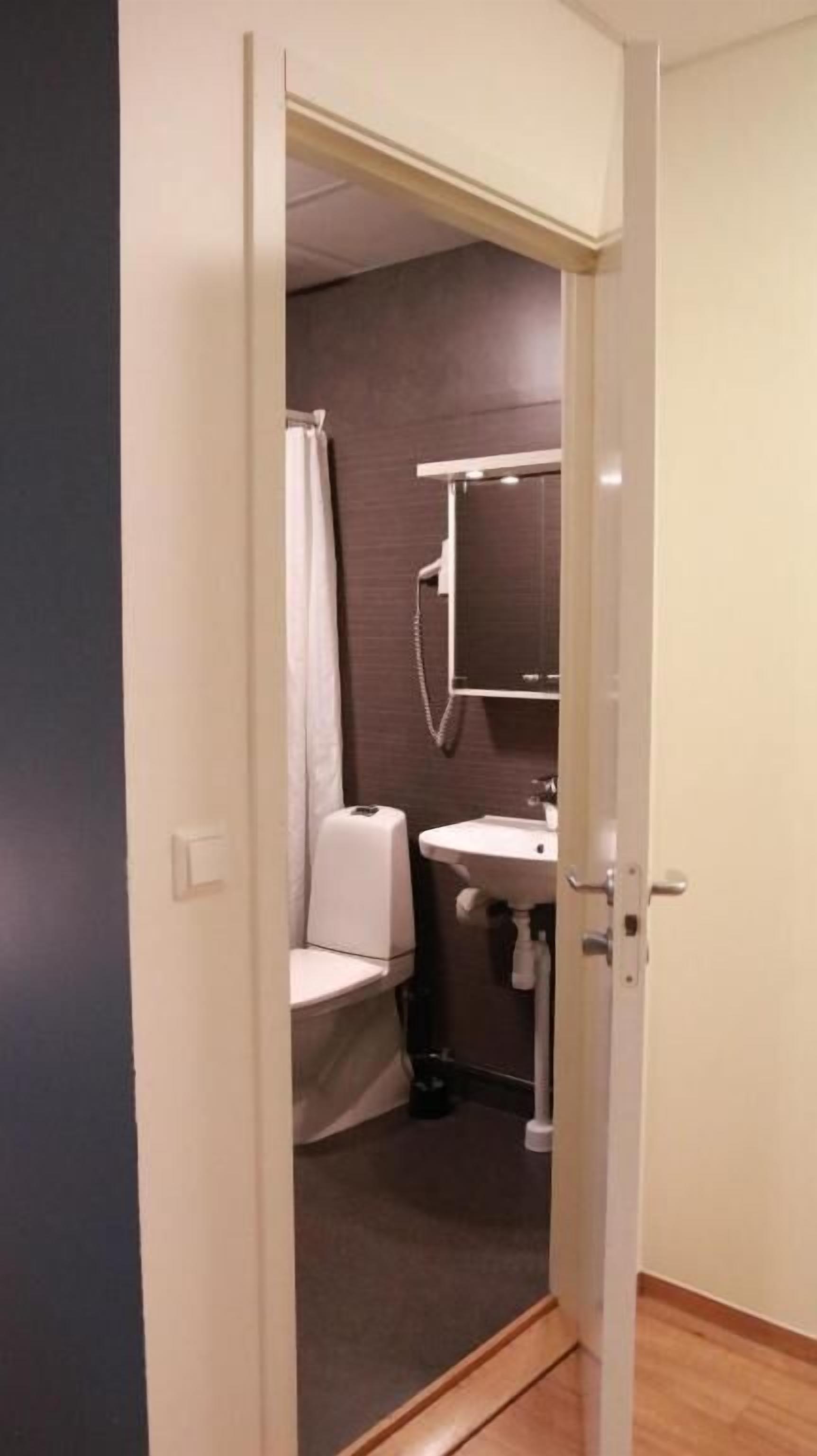 Un estrecho pasillo conduce a un baño con inodoro, lavamanos y cortina de ducha.