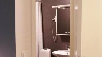Un estrecho pasillo conduce a un baño con inodoro, lavamanos y cortina de ducha.