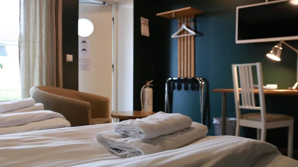 A hotel room with a bed, a chair, a desk with a lamp, and a TV.