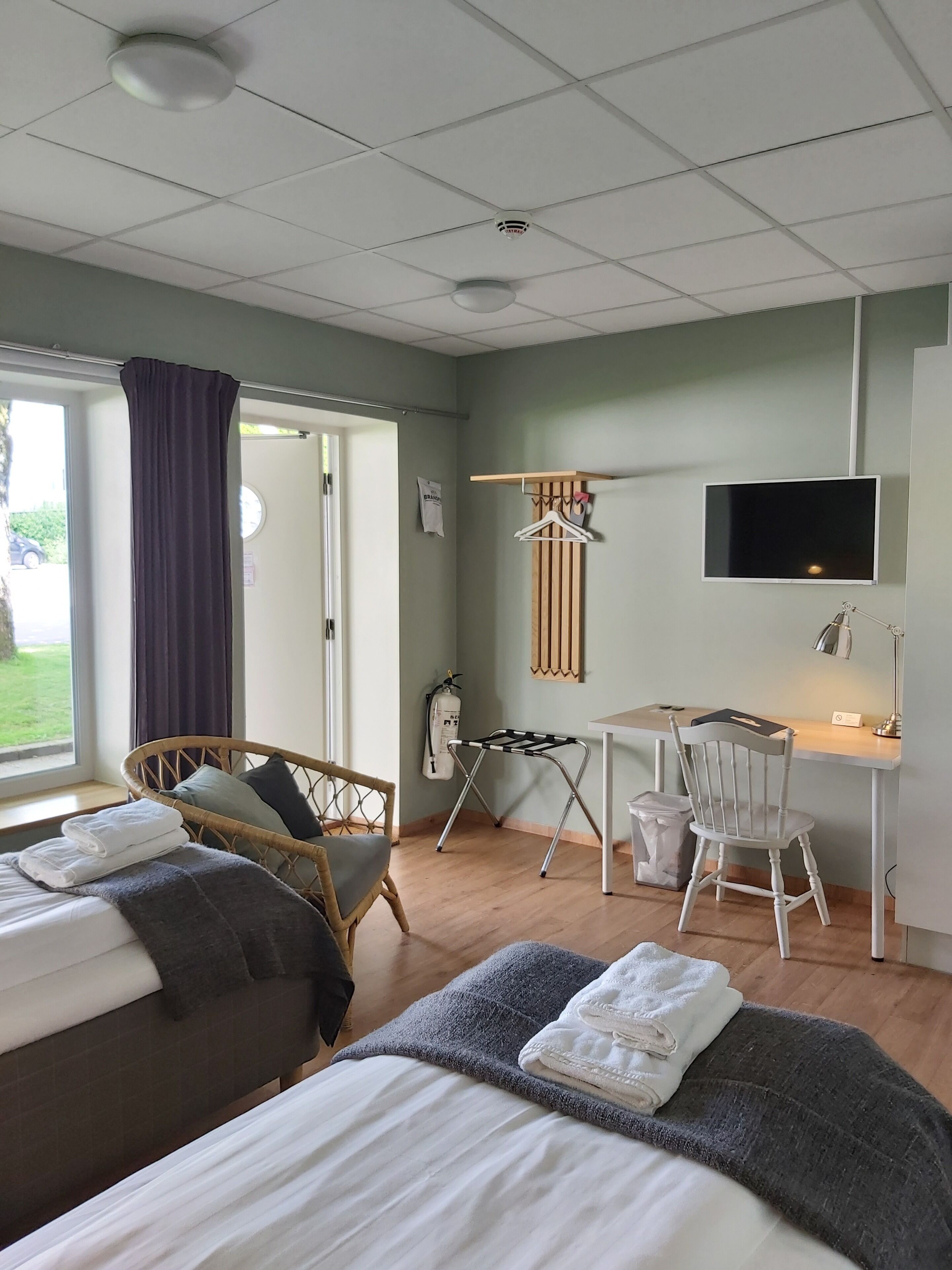 A hotel room with two beds, a desk, a chair, a TV, and a window with curtains.