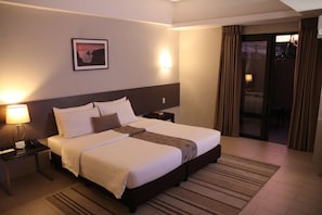 A hotel room with a large bed, bedside tables, a nightstand, a lamp, a picture on the wall, and a view through the door.