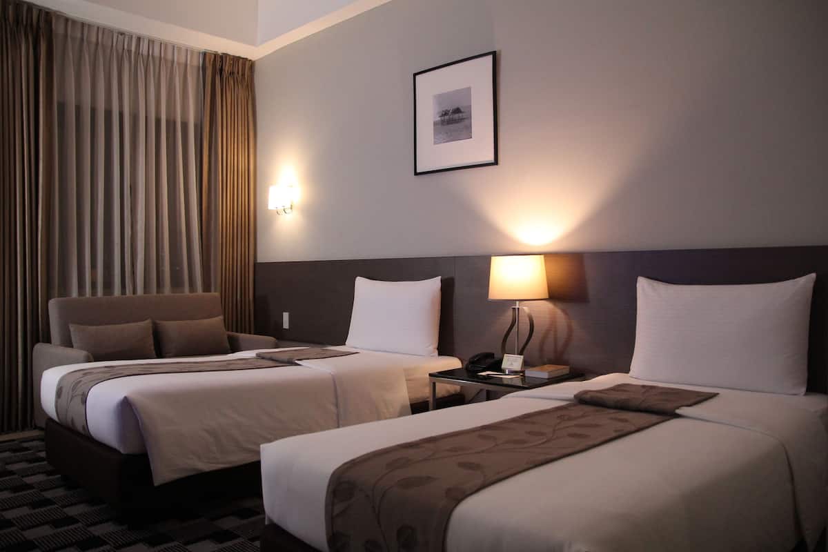 A hotel room with two beds, a desk, a chair, a lamp, and a framed picture on the wall.