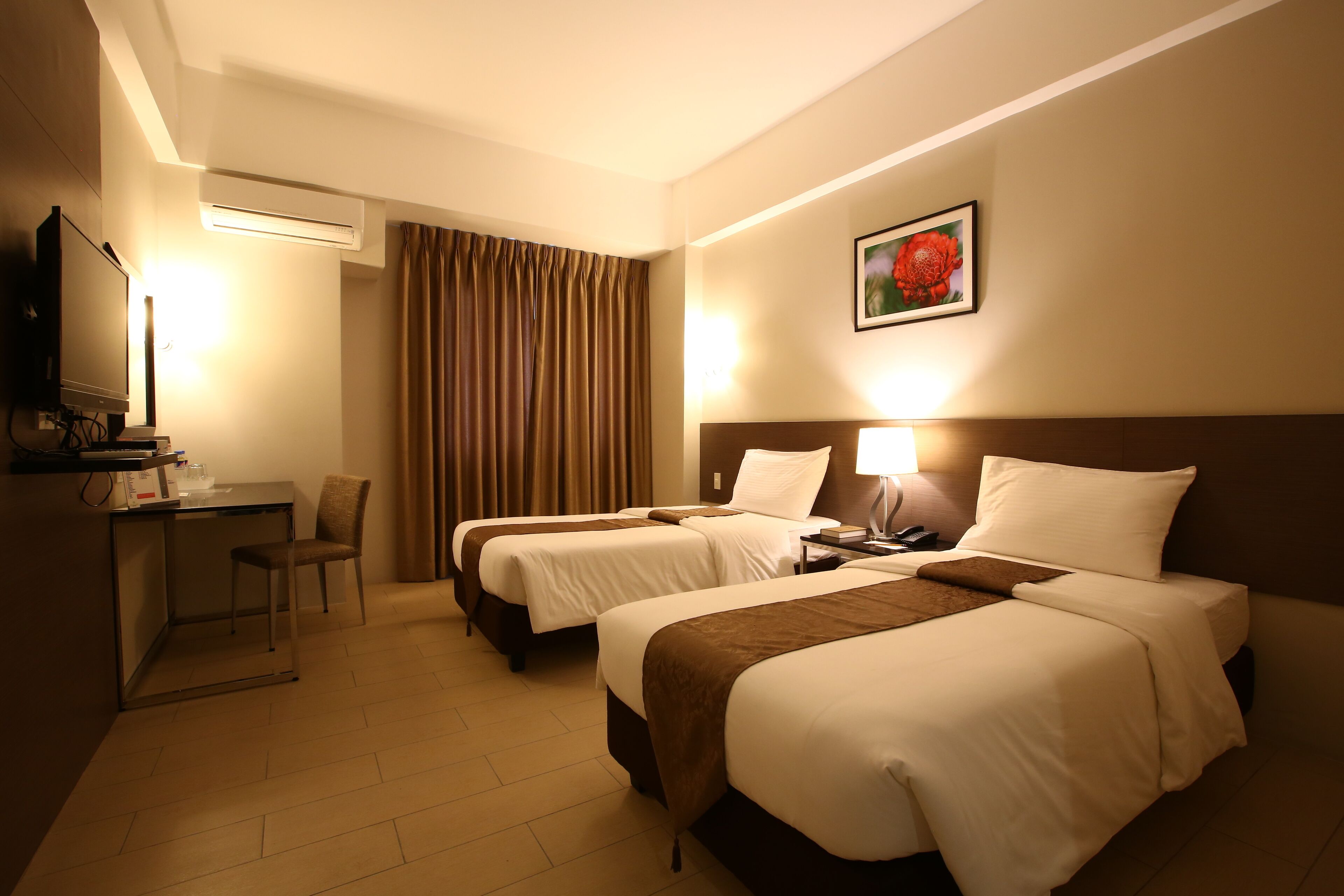 A hotel room with two beds, a desk, a chair, a TV, and a painting on the wall.