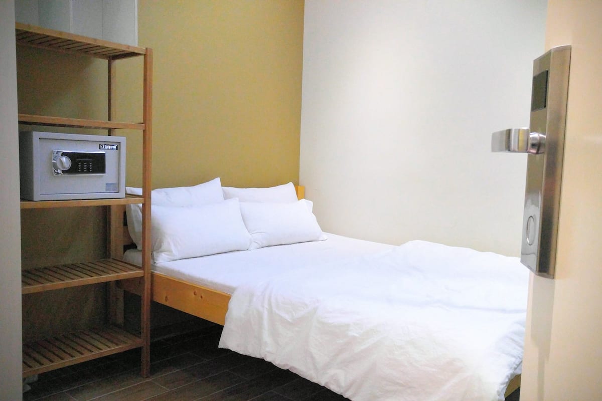 Cama pequena e bem arrumada com roupa de cama branca num quarto compacto.