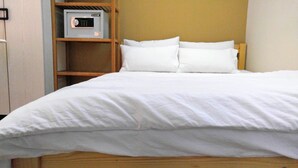 A bed with white bedding, a wooden headboard, and a safe on a shelf to the left. - Nuts Hotel (Kowloon)