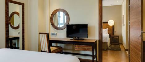 A hotel room with a bed, a desk with a television, a mirror, and a door leading to another room.
