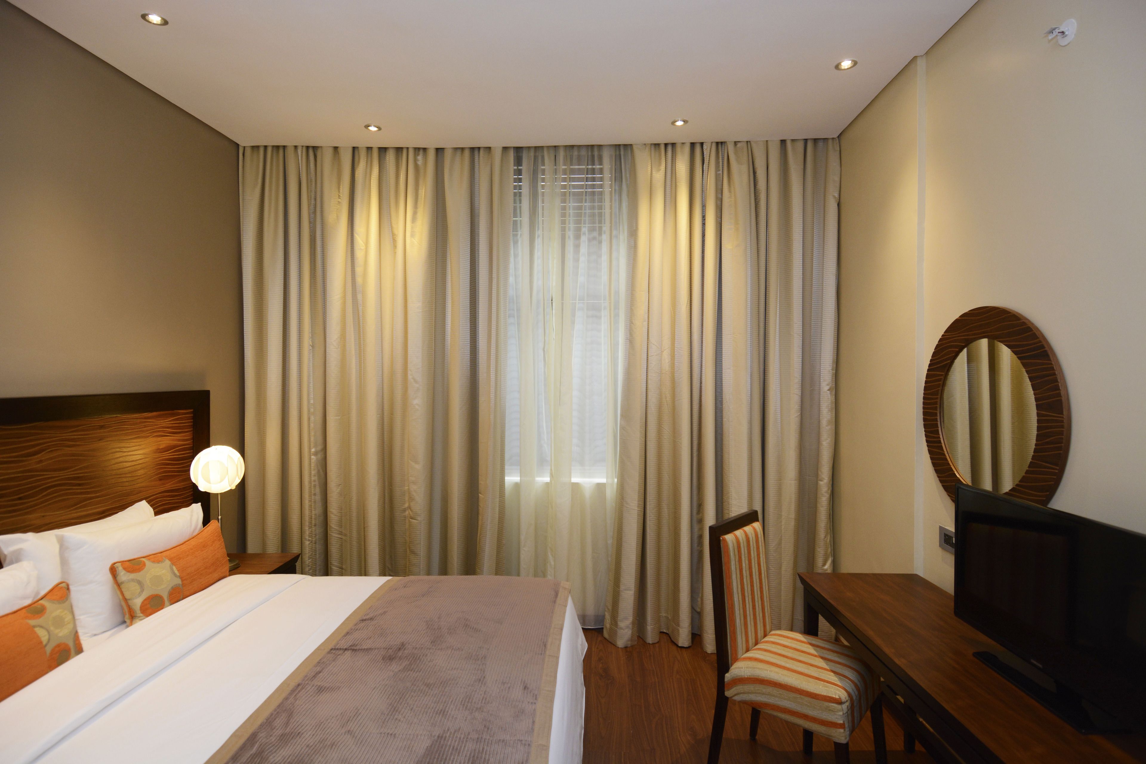A hotel room with a bed, a desk, a chair, a television, and a large window with curtains.