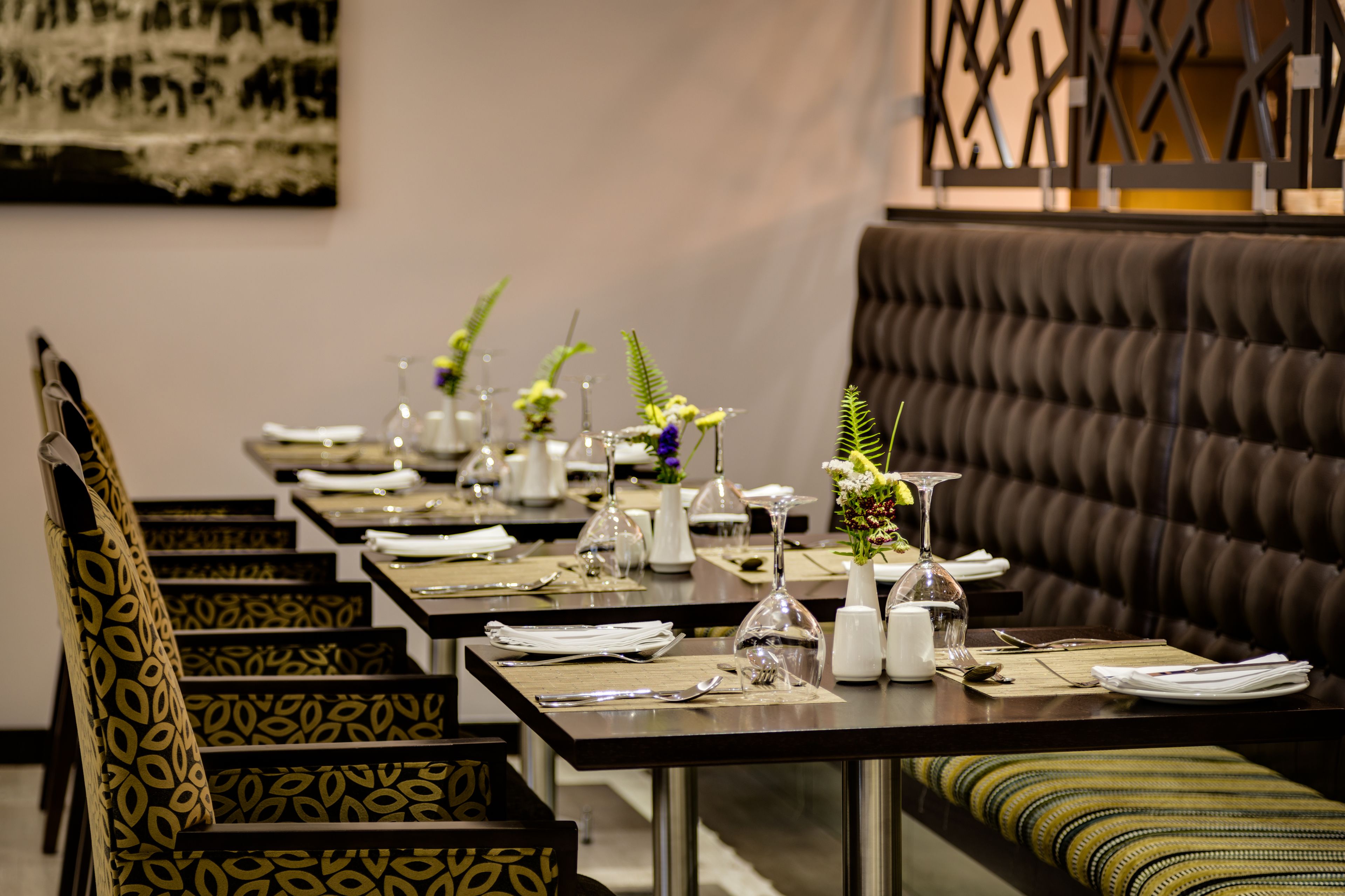 A restaurant with a long dining table set with white plates, silverware, and glassware. There are vases with flowers on the table, and a brown upholstered bench is visible in the background.