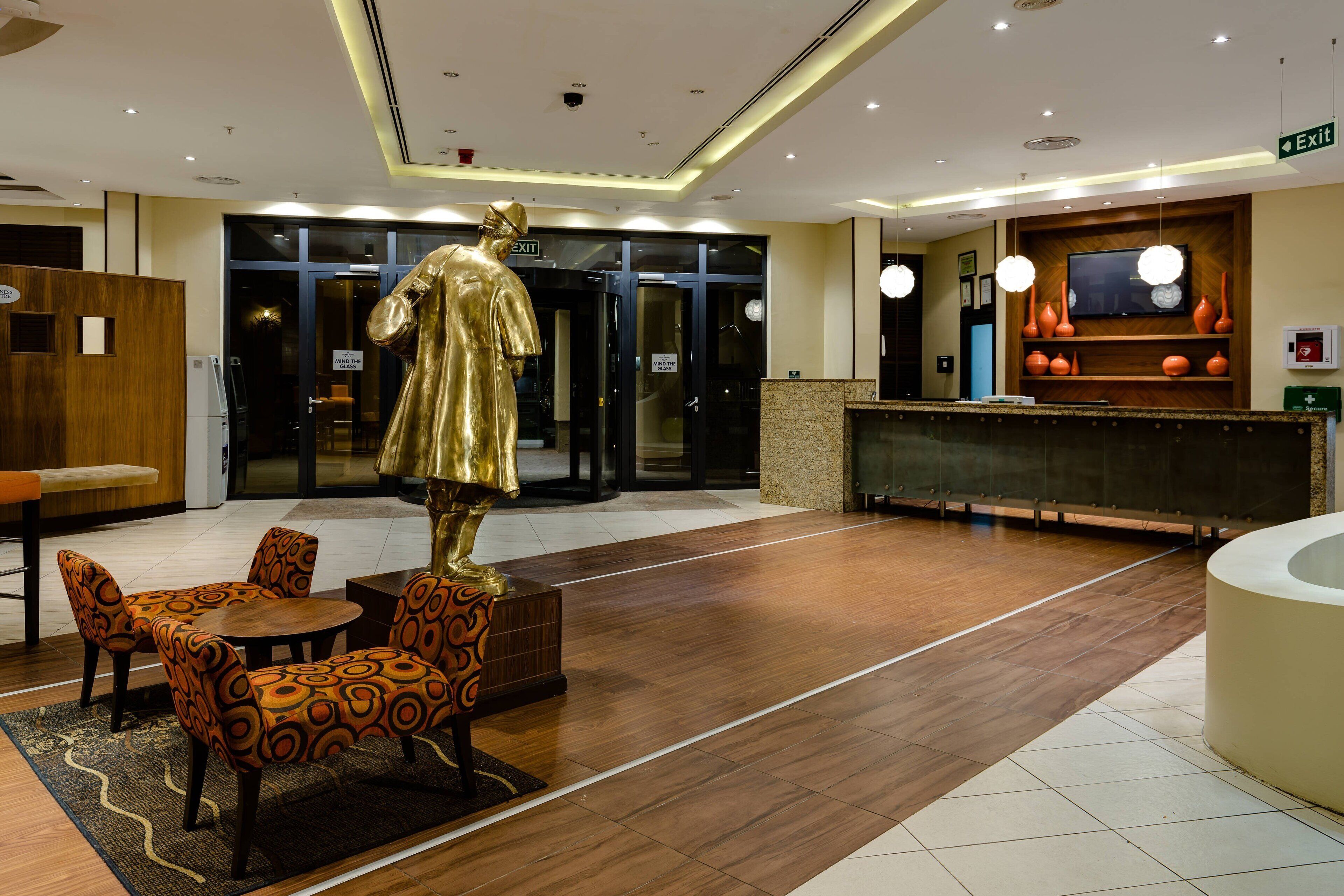 A hotel lobby with a reception desk, a statue, seating area, and a TV mounted on the wall.