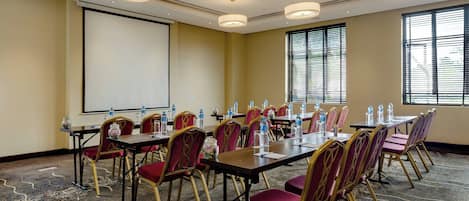 Un salón de conferencias con mesas, sillas y una pantalla para proyector.