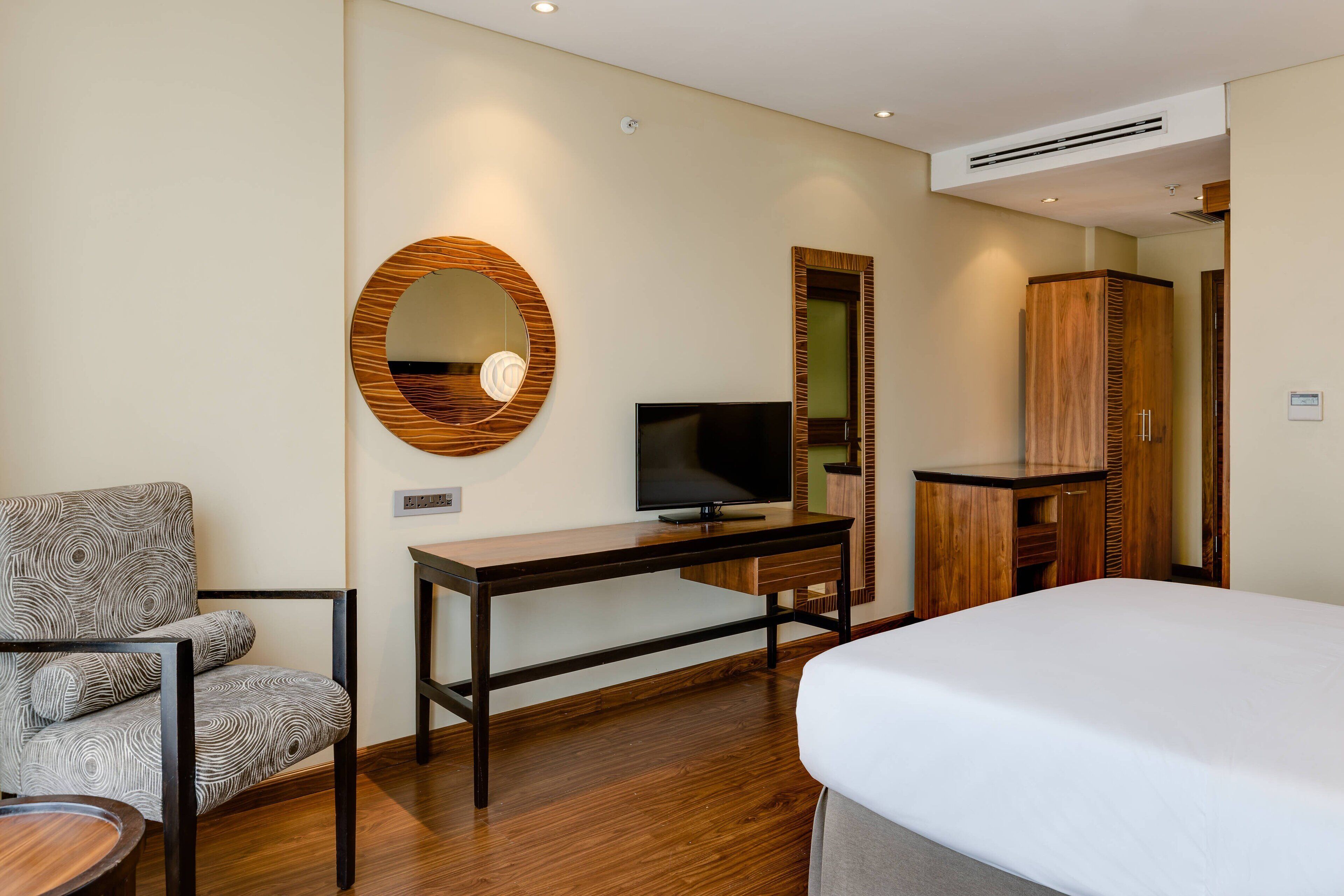 A hotel room with a bed, a TV, a desk, a chair, and a wardrobe.