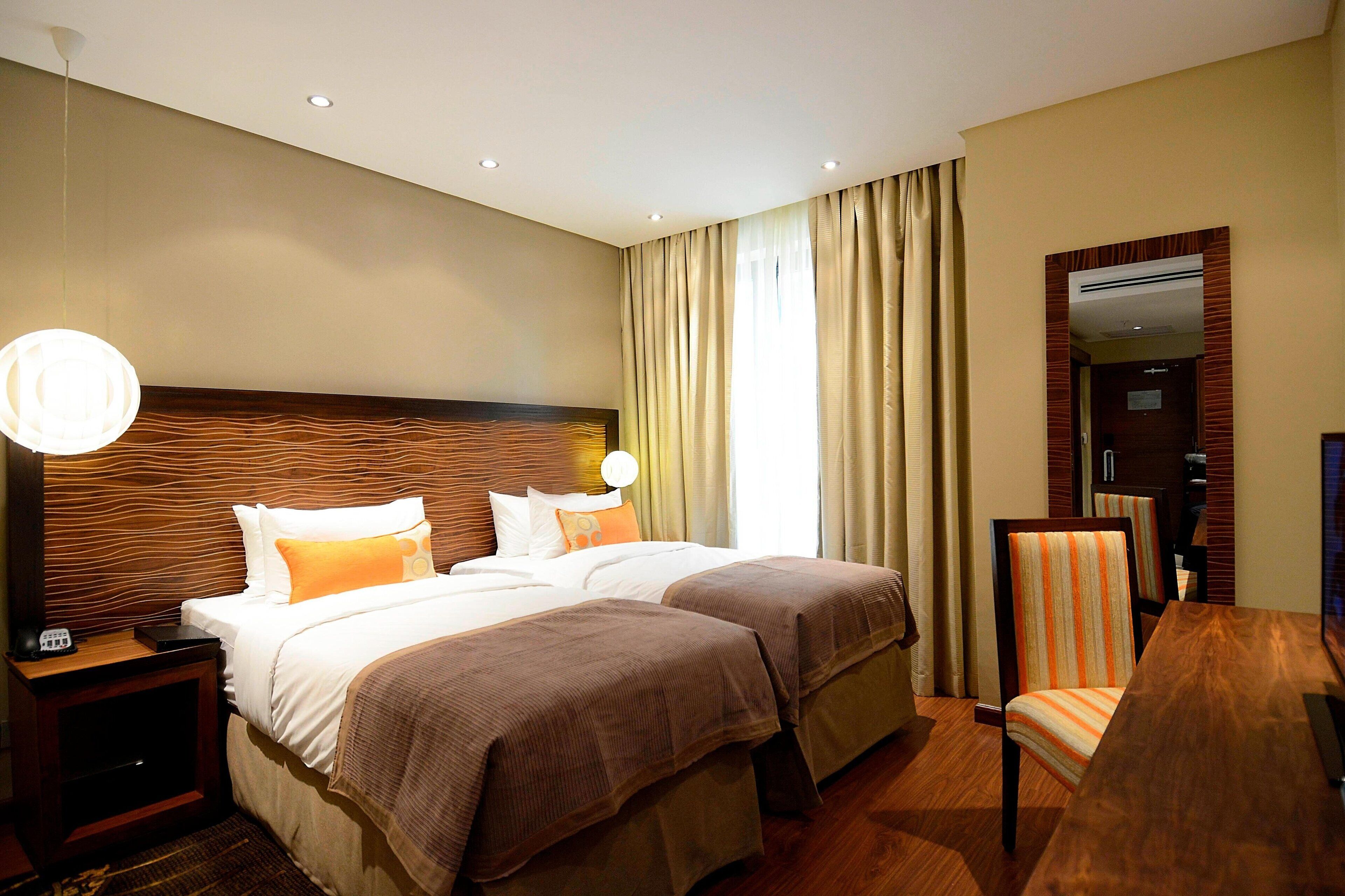 A hotel room with two beds, a wooden headboard, a desk with a chair, and a large mirror.