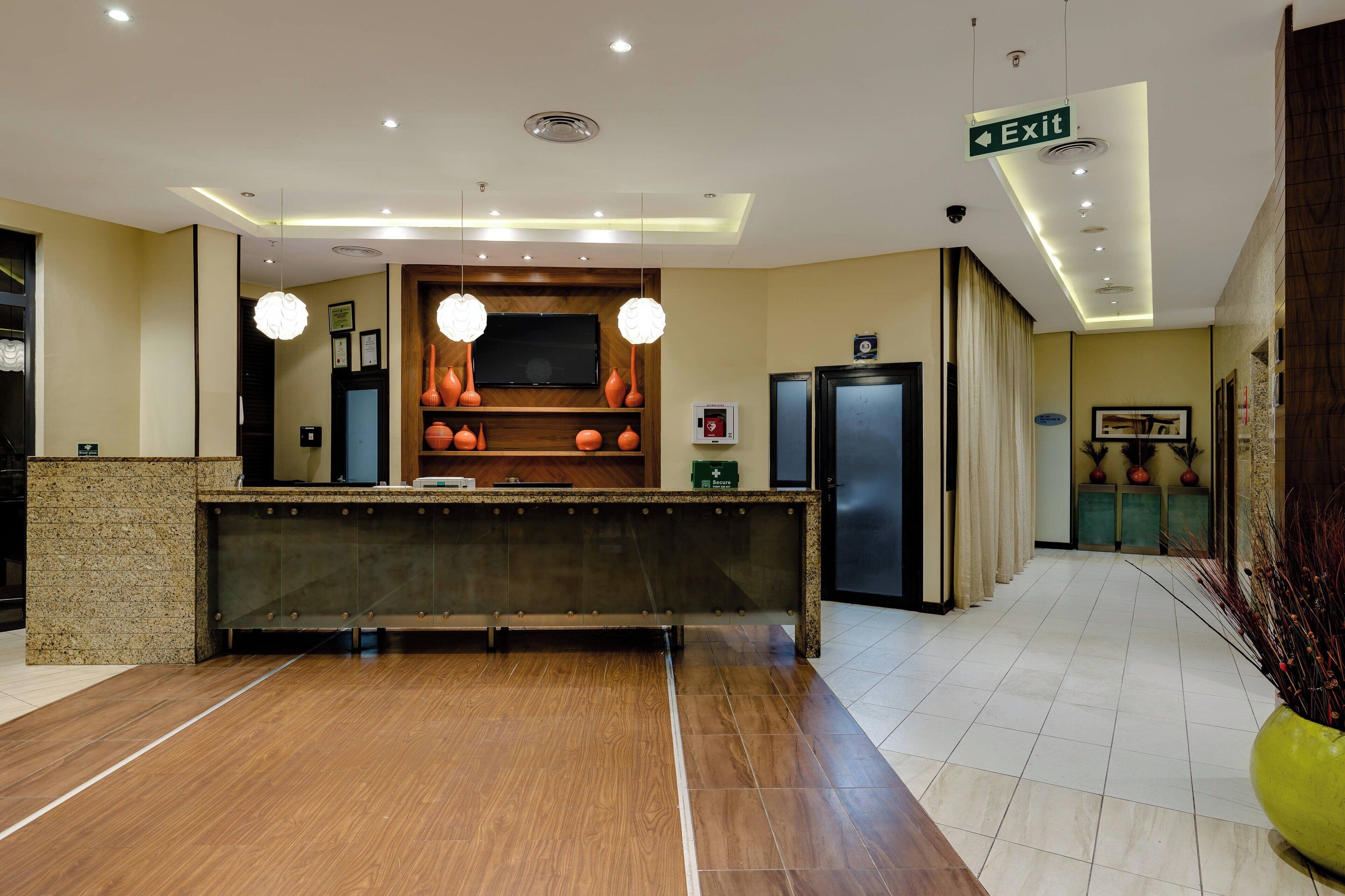 Un espace d’accueil d’hôtel avec un comptoir de réception en bois, un téléviseur et un panneau indiquant la sortie.