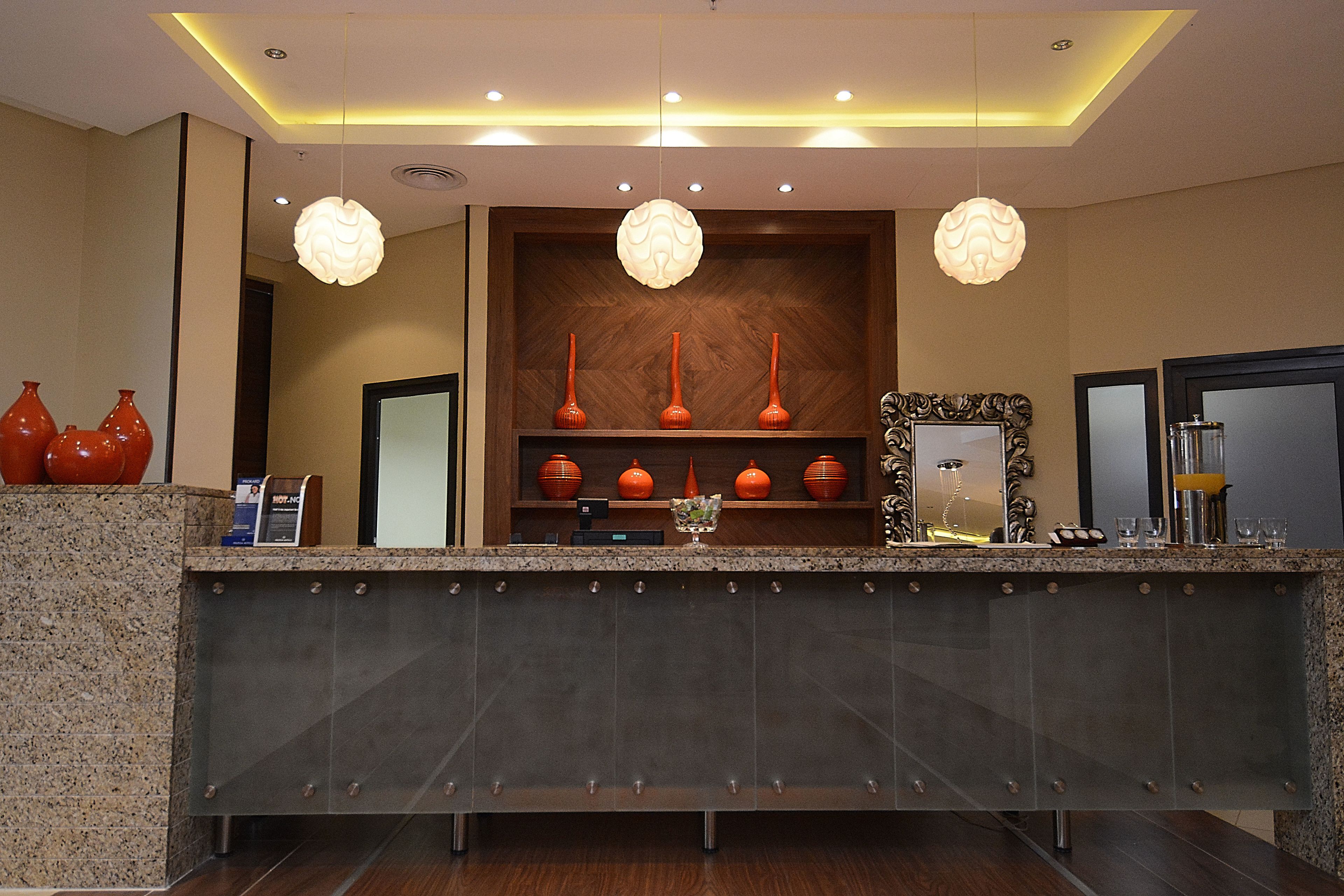 Zona de recepción con mostrador de mármol, tres jarrones naranjas en estantes y un espejo con marco decorativo.