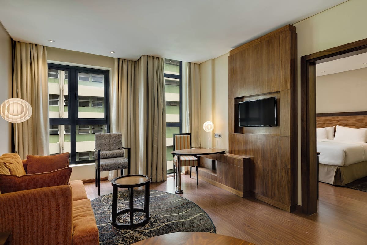 A hotel room with a sofa, armchairs, a small table, a TV, and a bed.